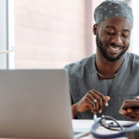 Physician wearing scrubs sitting at his laptop taking a medical survey for money.