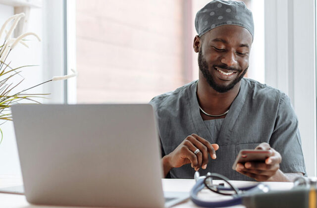 Physician wearing scrubs sitting at his laptop taking a medical survey for money.