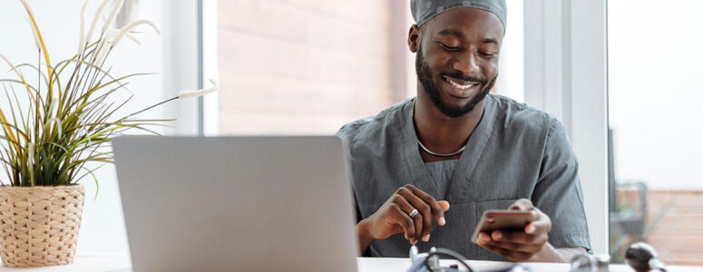 Physician wearing scrubs sitting at his laptop taking a medical survey for money.