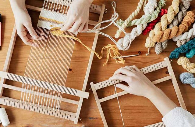 Hands of two professional crafters weaving a rug to sell for profit