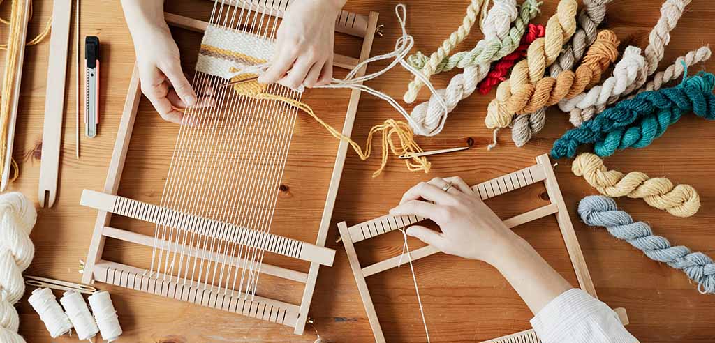 Hands of two professional crafters weaving a rug to sell for profit