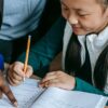 Student holding a pencil and a teacher pointing to the student's workbook