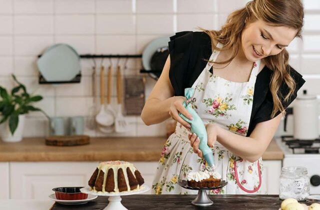 Baker at home wearing a floral apron and frosting a cake