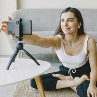 Content creator or influencer sitting cross-legged and setting up a phone on a tripod to film new content