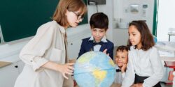 Teacher in a classroom showing three students different countries on a globe
