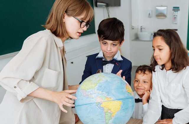 Teacher in a classroom showing three students different countries on a globe