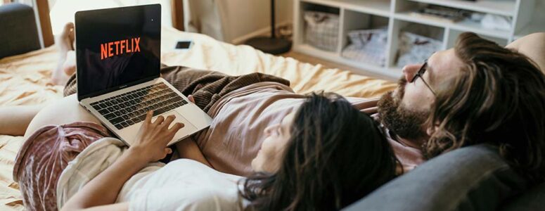 Woman lying on her bed watching Netflix on her laptop.