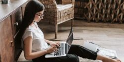 Freelance writer sitting on the floor working on a project on her laptop.