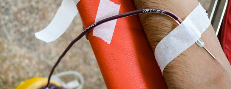 Close view of a donor's arm as they give blood plasma at a clinic.