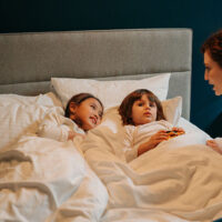 Overnight babysitter telling a bedtime story to two children who are lying in bed