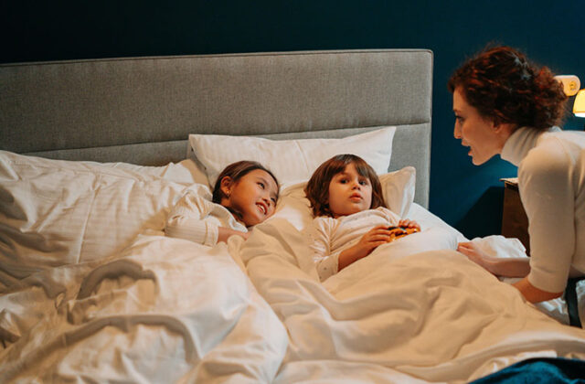 Overnight babysitter/nanny telling a bedtime story to two children who are lying in bed