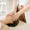 Hands of a professional massage therapist giving a head massage to a client who's lying on a massage table