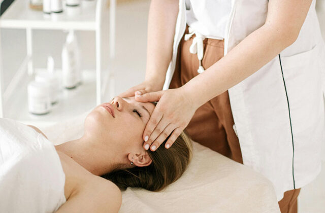 Hands of a professional massage therapist giving a head massage to a client who's lying on a massage table