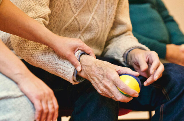 Professional caregiver resting a supportive hand on the arm of a client who's squeezing a physical therapy ball