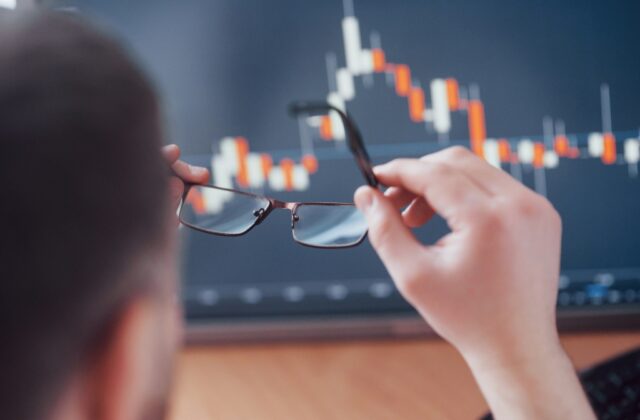 Man putting on spectacles to view investment data on a computer.