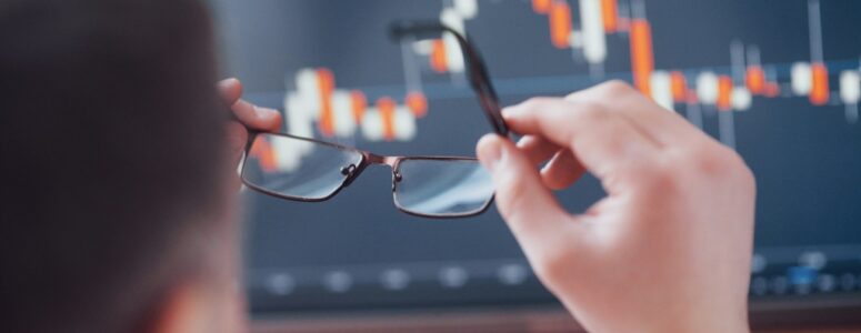 Man putting on spectacles to view investment data on a computer.