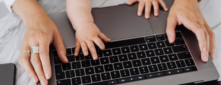 Closeup of a baby and parents' hands on a laptop keyboard.