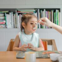 Babysitter feeding a toddler at a dining table
