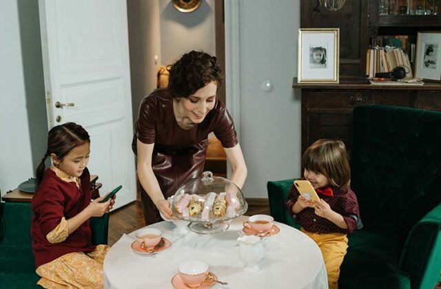 Babysitter setting cake on a table where two children are having a tea party