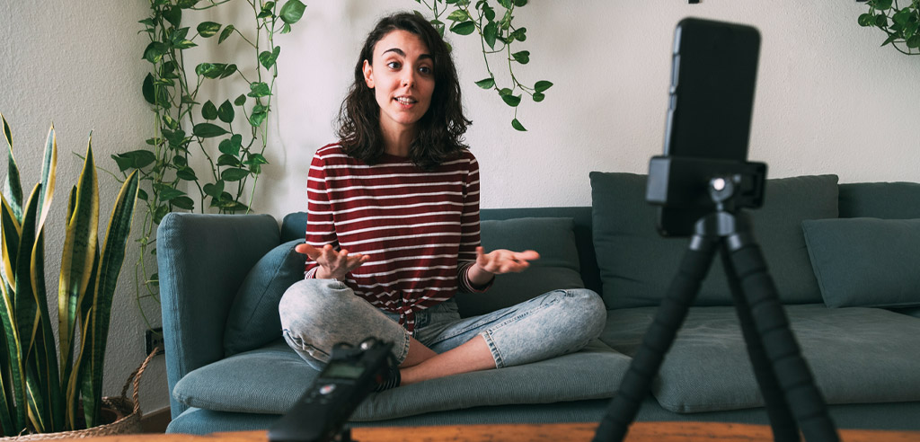 Woman sitting on a touch talking into a camera for her vlogging side hustle