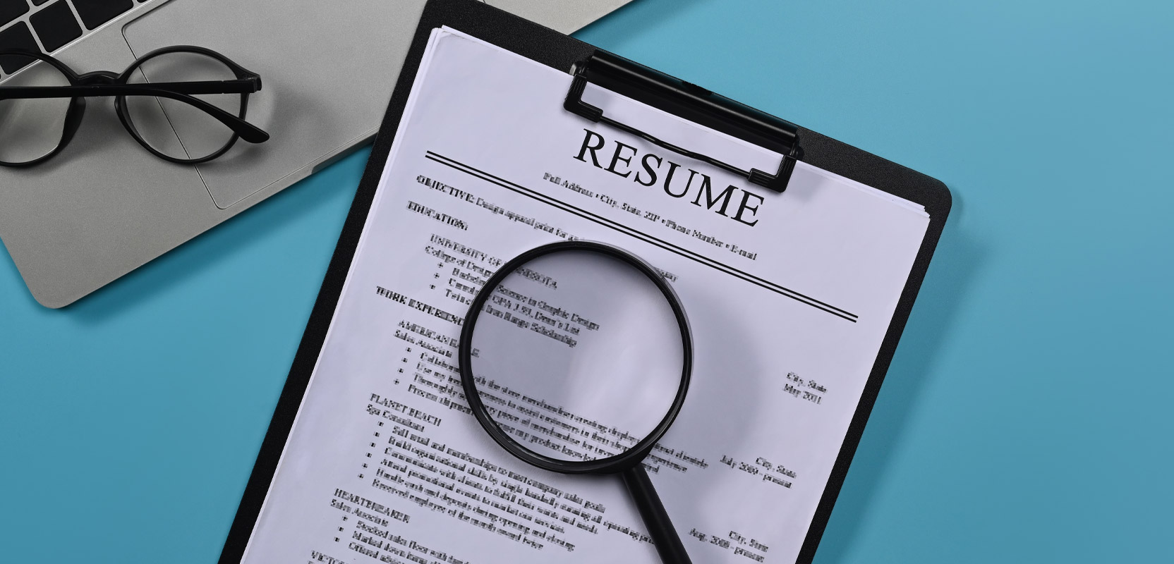 Magnifying glass resting on a resume on a clipboard