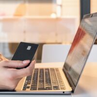 Woman sitting at her laptop with her phone using Fetch to save money.