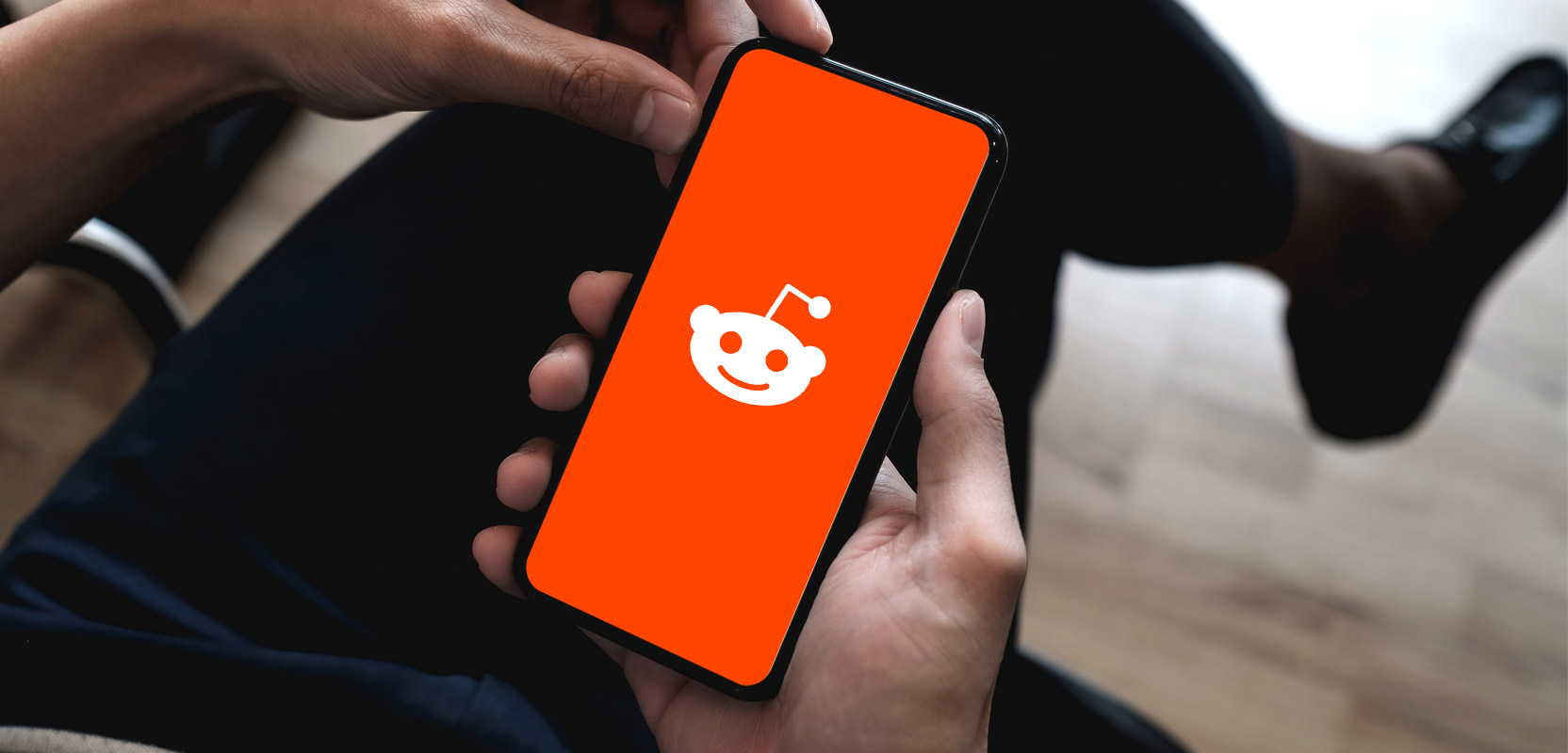Closeup of someone holding a smartphone with the Reddit logo on it