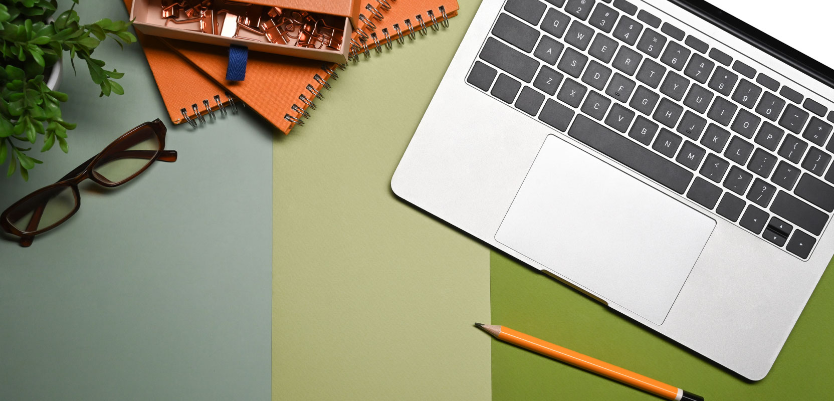 Top view of a laptop, a pencil, and several spiral-bound notebooks on a striped green surface