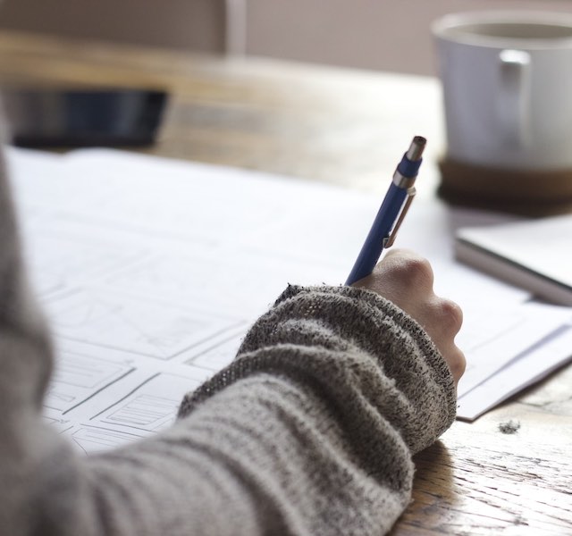 Close view of a writer at their desk holding a pen and working on an article.