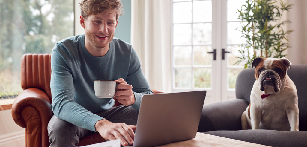 Man sitting at his laptop next to his pet dog and working on his full-time remote job from home