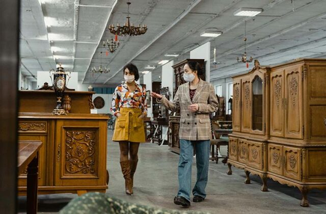 Two furniture flippers browsing antiques in a large store for resale.