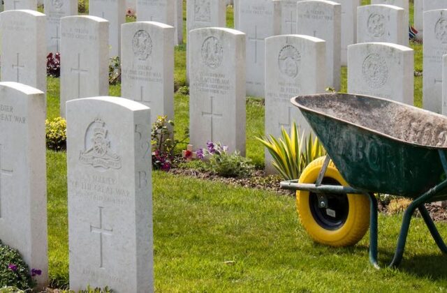 Close view of a gravestone in a cemetery with a wheelbarrow in the background.