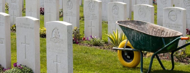 Close view of a gravestone in a cemetery with a wheelbarrow in the background.
