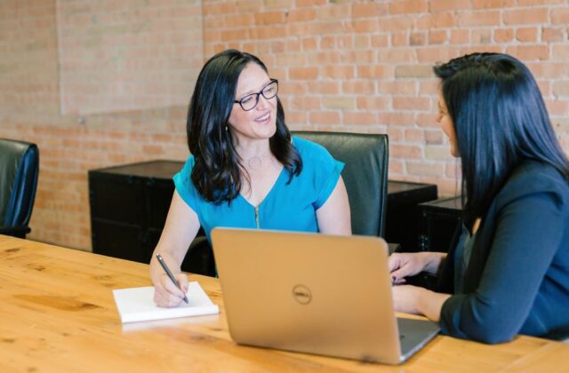 Professional consultant sitting in a meeting room with a client, with a laptop, notepad, and pen on the table