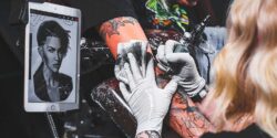 White-gloved hands of a professional tattoo artist using a tattoo needle to draw a tattoo on a client's arm