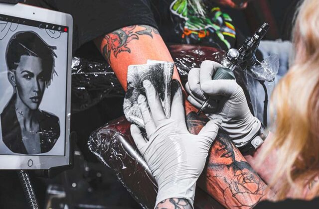 White-gloved hands of a professional tattoo artist using a tattoo needle to draw a tattoo on a client's arm