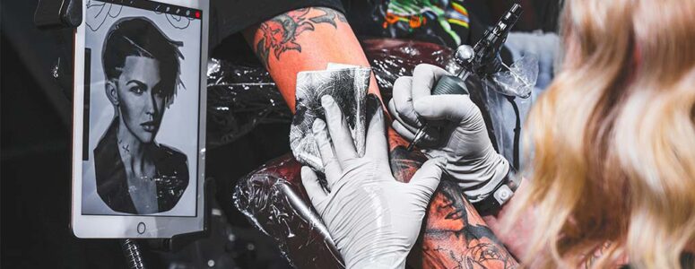 White-gloved hands of a professional tattoo artist using a tattoo needle to draw a tattoo on a client's arm