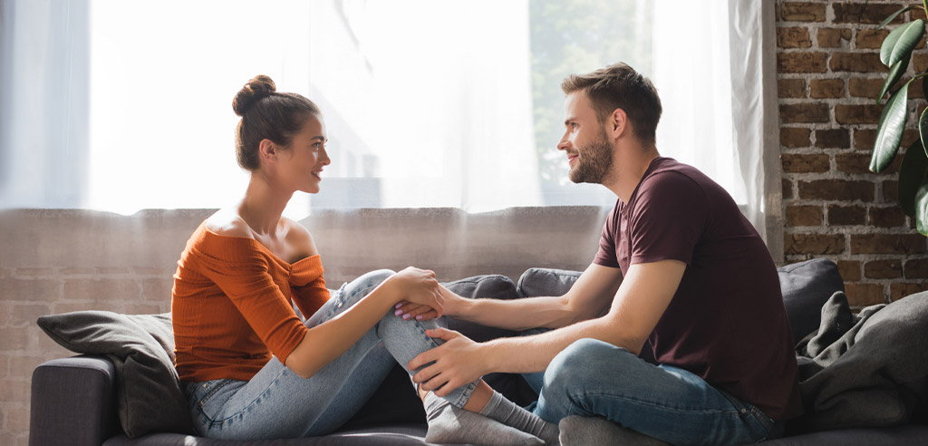 Man and woman sitting on a couch holding hands, smiling and making a plan to get out of debt