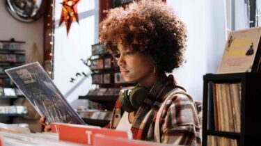 Young person in a music store, earphones around their neck, reading the back of a record