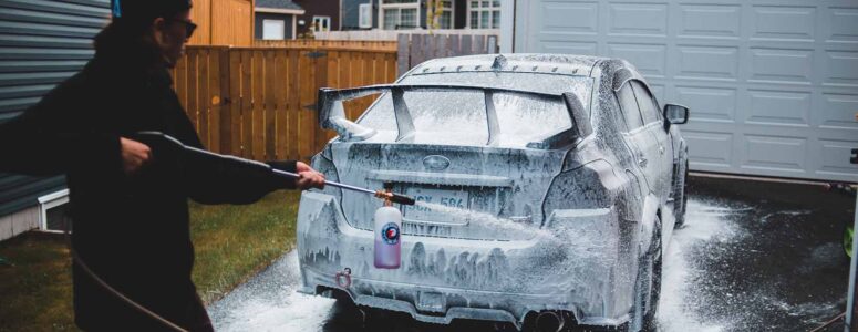 Car wash business owner hosing down a car in a driveway.