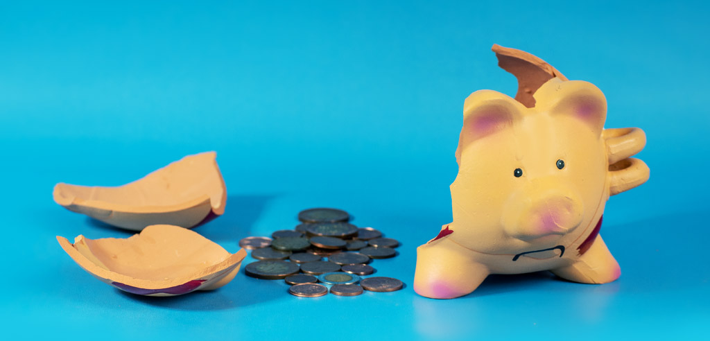 Pieces of a broken piggy bank surrounding a pile of coins