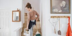 Professional house cleaner at a client's home carrying a broom and cleaning supplies