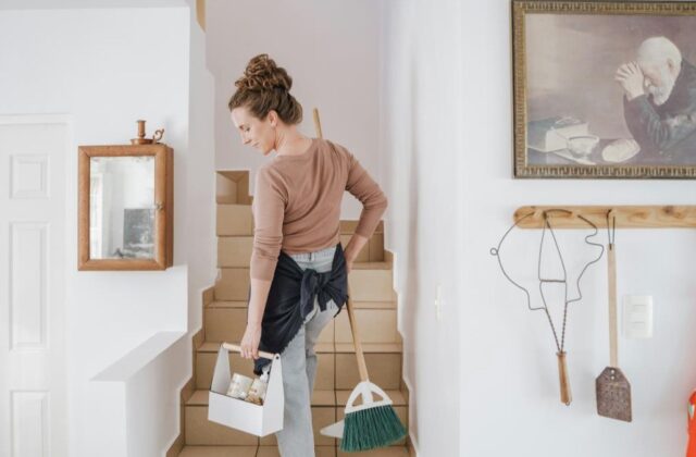 Professional house cleaner at a client's home carrying a broom and cleaning supplies