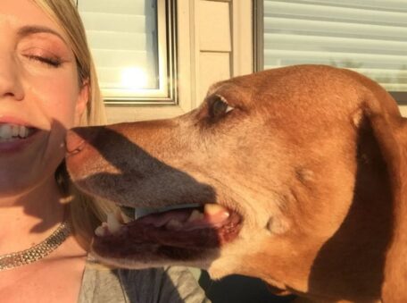 Professional pet sitter Jennifer D. smiling in the sunshine with a brown dog