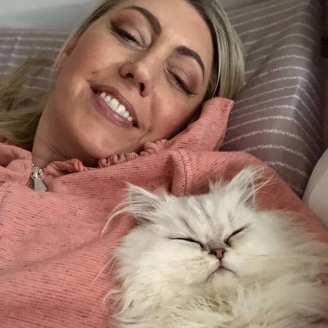 Professional pet sitter Jennifer D. in a pink hoodie holding a fluffy white cat
