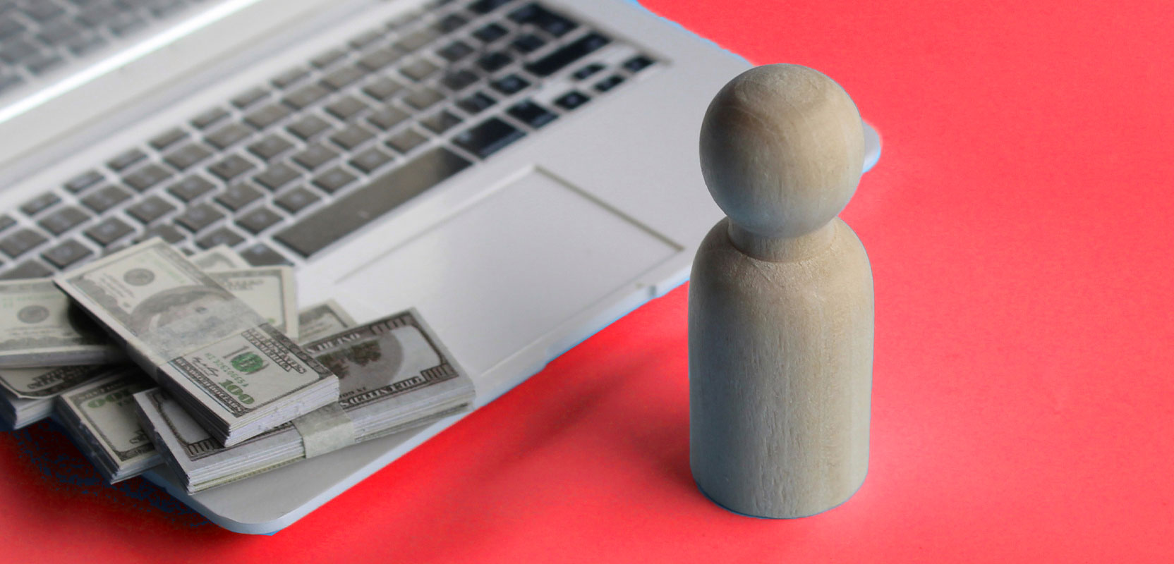 Carved wooden object standing in front of a laptop with a pile of money on the keyboard