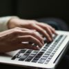 Close view of a medical transcriptionist's hands on their laptop.