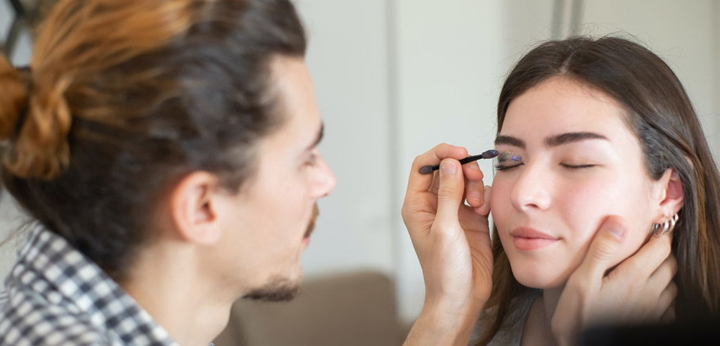 Male makeup artist applying eye makeup to a female client