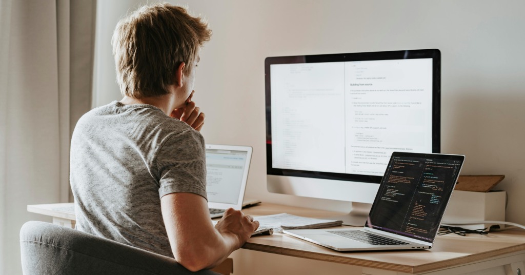 An overemployed worker switching betweeen different applications on several screens. 