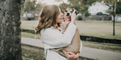 a pet sitter in a white sweater hugging a small, brown dog
